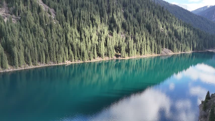 Drone footage capturing reflections of clouds and forests on the calm surface of a mountain lake.