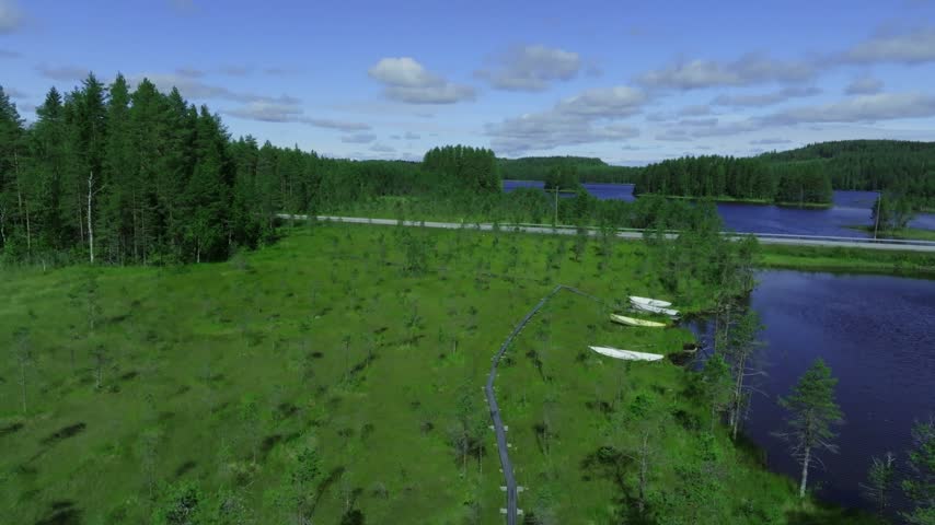 Aerial view of Koli National Park featuring a wooden boardwalk, lush forest, and calm lake waters in Lieksa, North Karelia, Finland.