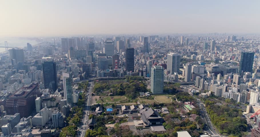 Aerial view of the Tokyo skyline featuring the historic Zojoji Temple, lush park grounds, and dense urban architecture under a clear sky in Tokyo, Tokyo, Japan.