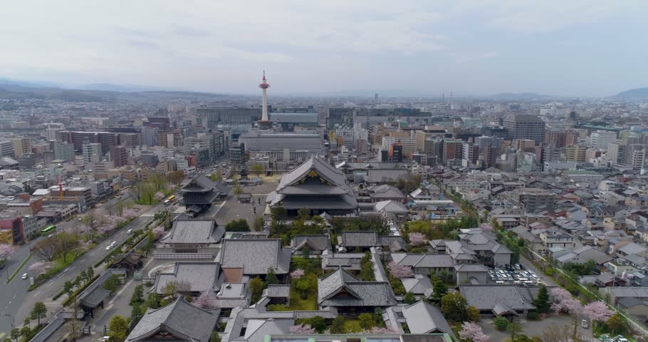 Aerial view of Higashi Hongan-ji Temple complex with traditional tiled roofs and Kyoto Tower rising in the background over the urban cityscape in Kyoto, Kyoto, Japan.