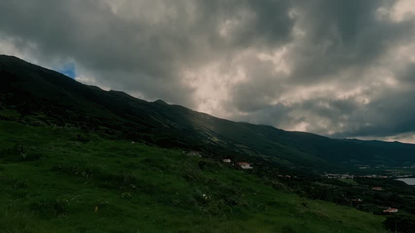 Dark Clouds Over Mountainous Green Landscape With Distant Houses