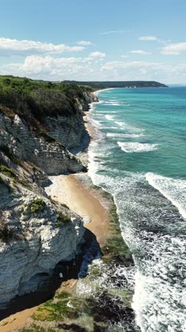 Aerial view of the rugged coastline with white cliffs, sandy beach, and turquoise sea waves crashing against the shore in Byala, Varna, Bulgaria.