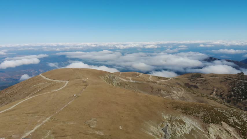 Aerial view of the Balkan Mountains ridge with winding dirt paths across dry grassy slopes above a sea of clouds in Gabrovo, Bulgaria.