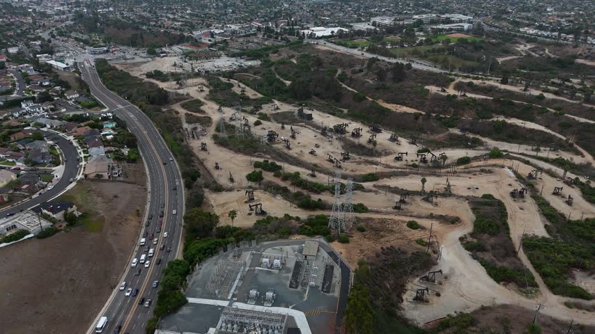 Aerial view of the Baldwin Hills oil field with numerous pump jacks, surrounding hills, and a busy highway in Los Angeles, California, United States.