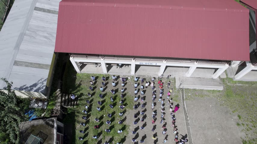 Aerial view of students standing in orderly rows in a school courtyard in front of a building with a red roof in Syapru Besi, Bagmati Province, Nepal.