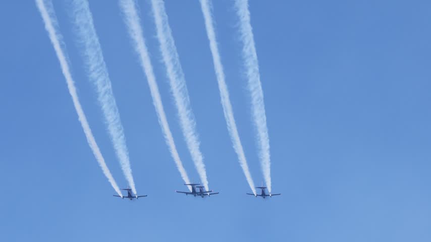 Dynamic aerial display featuring group of four high performance military aircraft flying in formation creating intricate smoke patterns during sunny day aviation exhibition.
