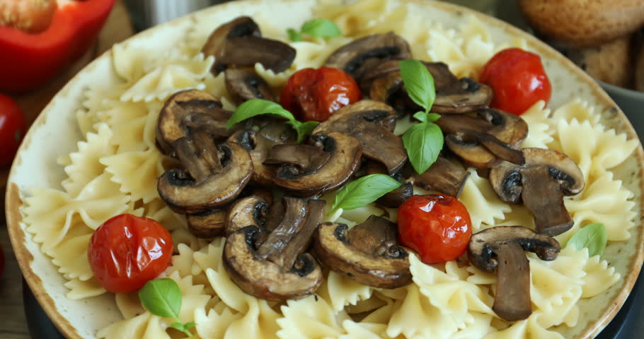 Tasty pasta with fried mushrooms, tomatoes and basil on table, closeup