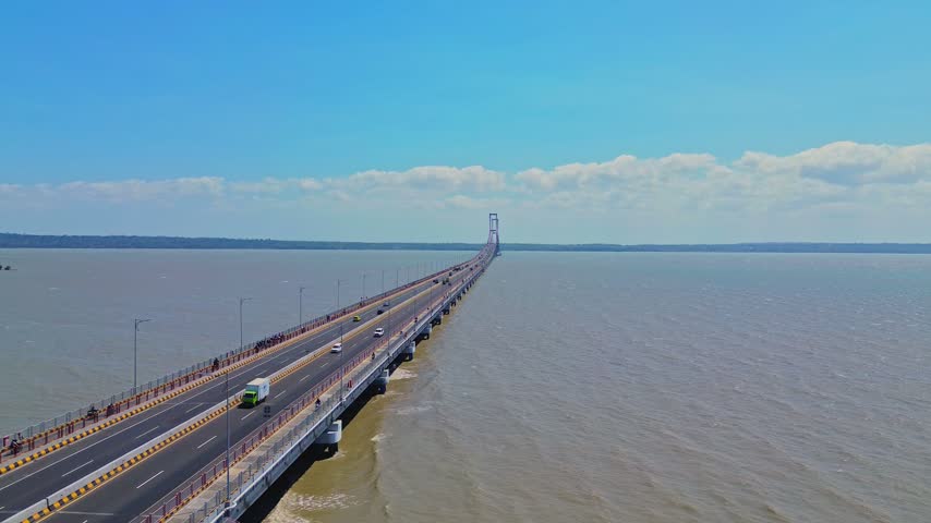 Aerial view of Suramadu Bridge spanning the Madura Strait with vehicles driving on the road under a clear blue sky in Surabaya, East Java, Indonesia.