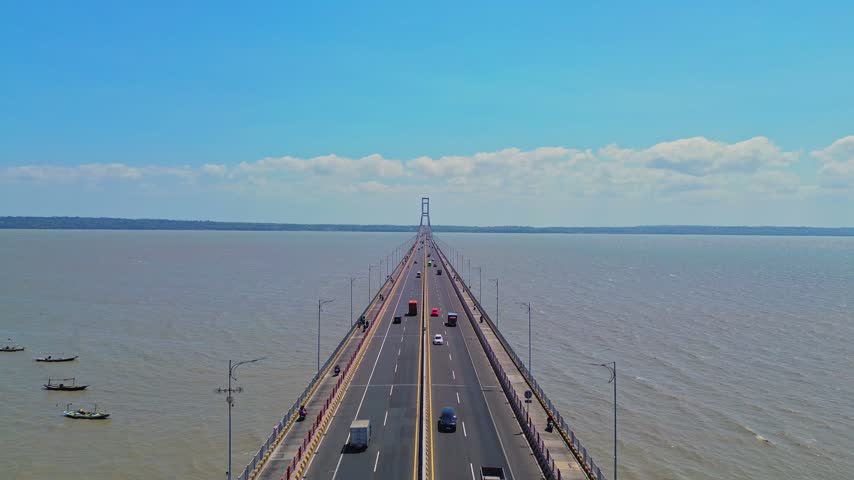 Aerial view of Suramadu Bridge with cars driving across the long span over the sea with small boats nearby in Surabaya, East Java, Indonesia.