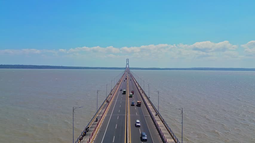 Aerial view of Suramadu Bridge spanning the Madura Strait with vehicles traveling across the lanes under a clear blue sky in Surabaya, East Java, Indonesia.