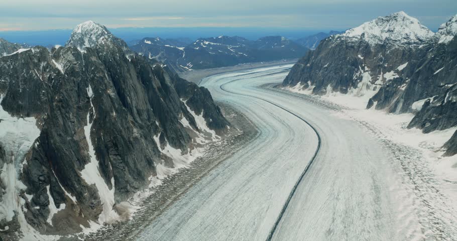 Aerial view of the massive glacier winding through the rugged snow-capped peaks of the Alaska Range in Denali Borough, Alaska, United States.