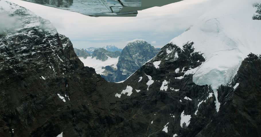 Aerial view of the rugged, snow-capped peaks of Mount McKinley seen from a small plane, with dramatic mountain ridges and glacial terrain in Denali Borough, Alaska, United States.