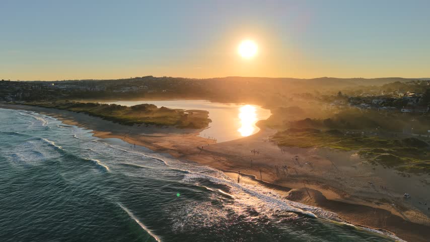 Aerial view of Dee Why Lagoon at sunset with golden light reflecting on the water, sandy beach, and coastal vegetation in Northern Beaches Council, New South Wales, Australia.