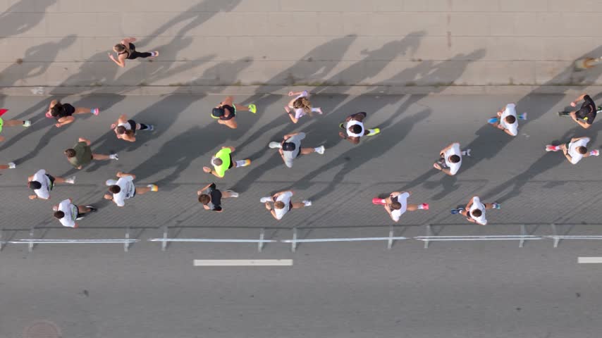 Aerial view of marathon runners racing along a city road with long shadows cast on the pavement in Kaunas, Kaunas County, Lithuania.