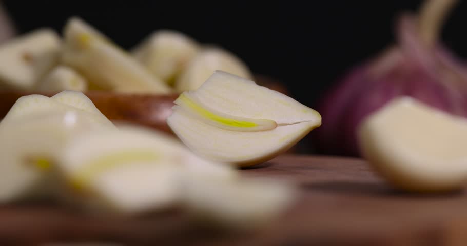 peeled and sliced purple garlic scattered on the black kitchen table and peeled and sliced, fresh and natural garlic spices scattered on the kitchen table during cooking