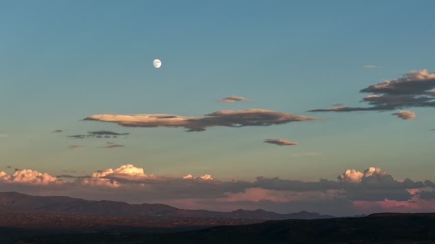 Aerial view of the moon rising over the southwestern landscape of Santa Fe during sunset with fading light and scattered clouds in Santa Fe, New Mexico, United States.