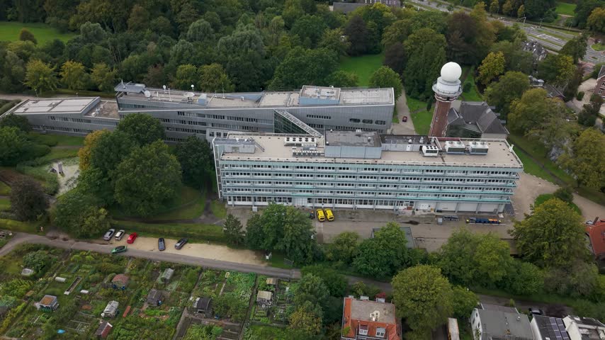 Aerial view of the KNMI headquarters featuring its distinctive weather radar tower and modern office buildings surrounded by lush greenery in De Bilt, Utrecht, Netherlands.