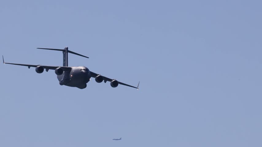 Military transport aircraft C-17 globemaster III in flight, cargo plane flying, heavy military aircraft, blue sky, wide shot, motion, aviation, air travel, cargo.
