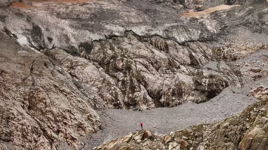 Aerial view of the rugged Presanella glacier with a person in a red jacket standing on a rocky outcrop in Giustino, Trentino-Alto Adige, Italy.