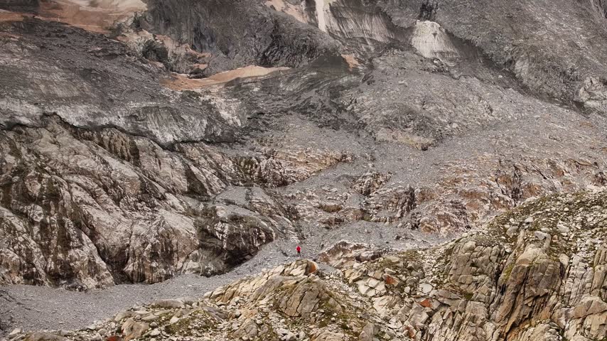 Aerial view of Presanella mountain slopes with rugged rocks and a hiker in a red jacket in Giustino, Trentino-Alto Adige, Italy.