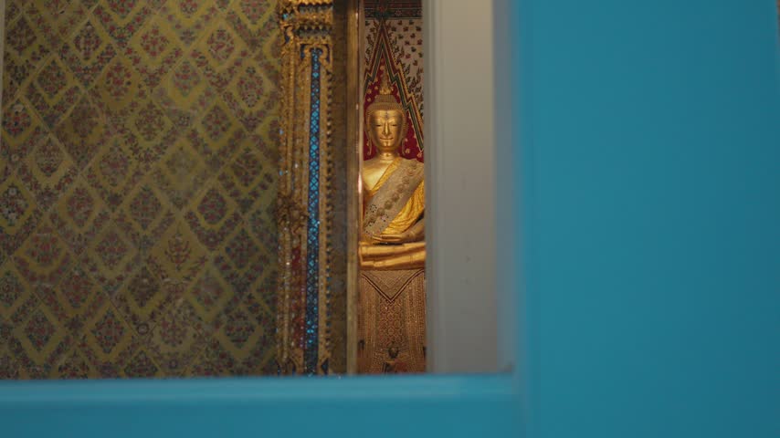 Golden buddha statue inside a temple in bangkok, thailand, seen through a blue window frame