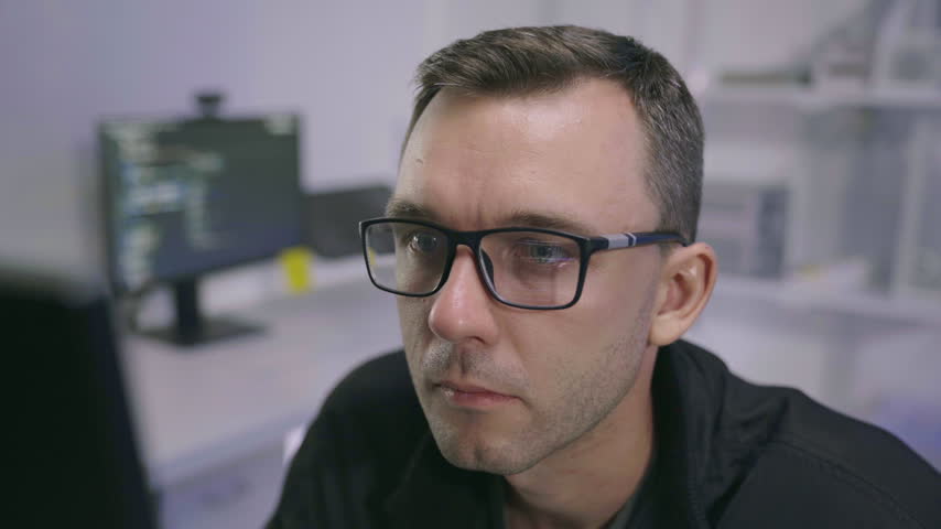 Close up of male software developer touching glasses while analyzing computer screen code, solving technical bugs in modern workspace.