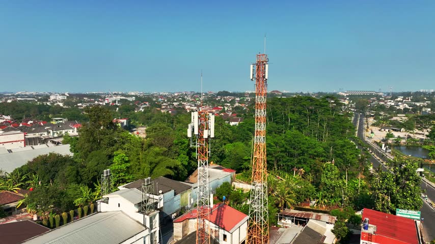 Tall telecommunications tower rising above a dense Indonesian urban neighborhood in a wide aerial cityscape