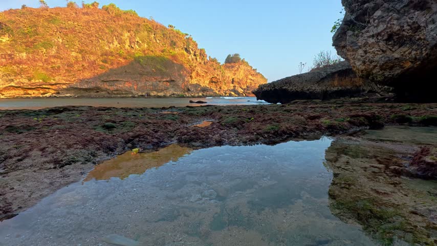 Rocky coastal cove with calm tide pool reflecting cliffs and blue sky during low tide