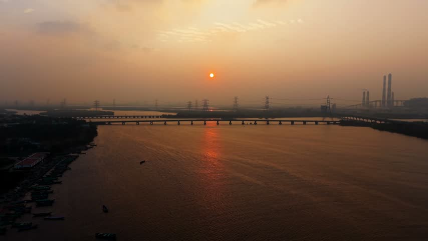 Aerial view of sunset over a river with power transmission towers and a bridge in the distance in India.