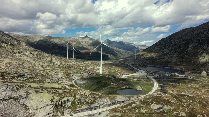 Aerial dolly forward past wind turbines in rocky Swiss Alps landscape.
