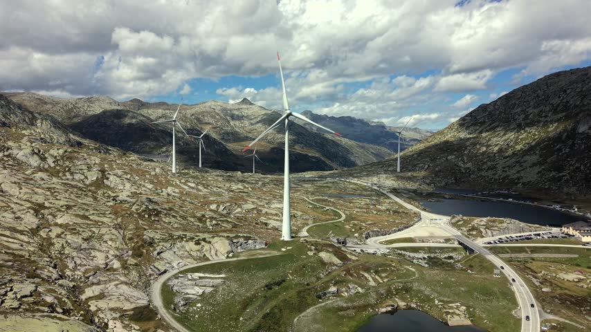 Aerial dolly forward past wind turbine in rocky Swiss Alps landscape.