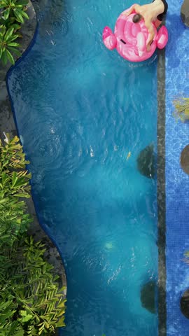 Top-down view of a man jumping onto a pink flamingo float, drifting in a swimming pool and falling into the water. Fun summer vacation, leisure and playful lifestyle concept.