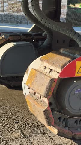 A close-up vertical shot of crawler tracks from heavy construction machinery sitting on a freshly milled asphalt road surface during roadworks.