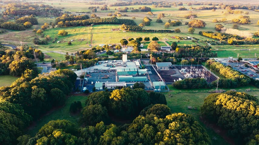 Aerial view of an industrial facility and power substation surrounded by macadamia orchards and farmland in Byron Bay, New South Wales, Australia.