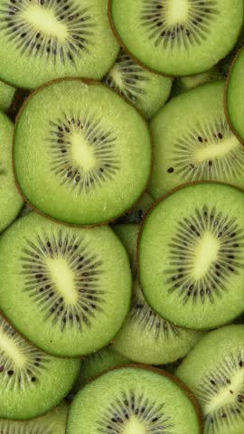 Close-up kiwi slices rotate in a vertical frame, revealing green flesh, seeds, and fresh texture.