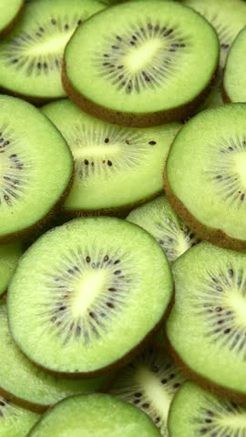 Fresh kiwi slices rotate in a vertical frame, forming a vivid green pattern with seeds and texture.
