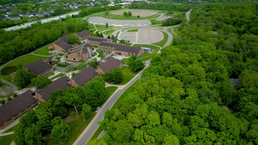 Expansive aerial footage showcasing a Oakland community college campus with modern architecture next to a lush forest in Farmington Hills, Michigan.