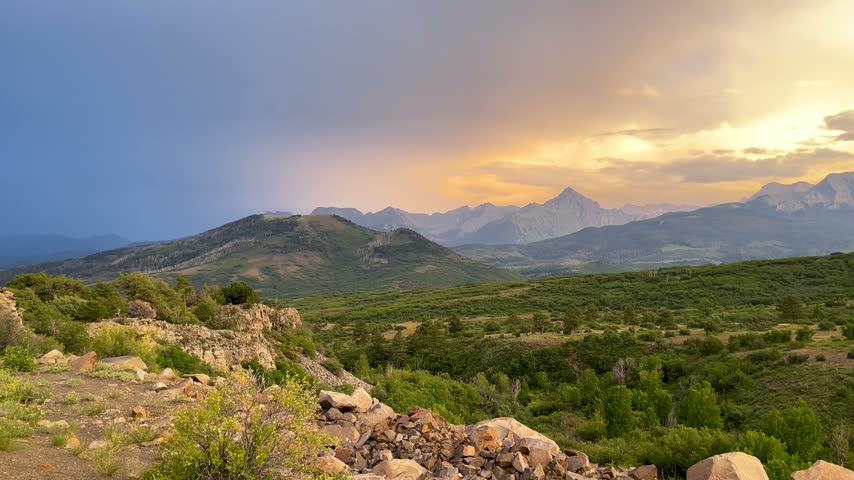 Dramatic sunset casting golden light over the lush green San Juan Mountains in Colorado.