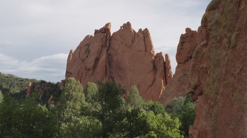 A static video of a large rock in the Rocky Mountains of Colorado inside the Garden of the Gods. It is red and orange, and the day is bright and sunny. There are green trees surrounding the rock.