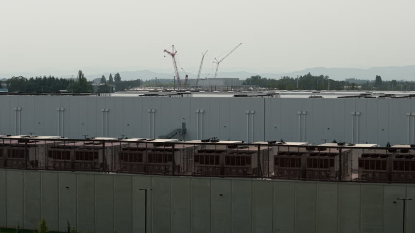 Large data center complexes in Hillsboro, Oregon with cooling units and large cranes on distant buildings. Slow drone rising shot.