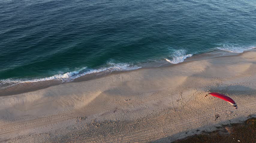 Aerial view of a powered paraglider landing on the beach in Itaipuaçu, Rio de Janeiro, Brazil.