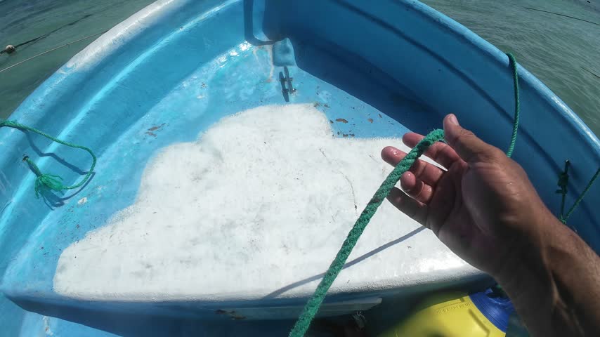 POV of a man handling a rope aboard a small boat, pulling in the line while preparing to leave shore and navigate the Caribbean Sea.