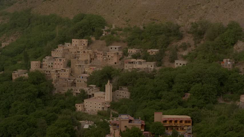 Cinematic landscape view of a terraced Berber village nestled into lush green mountain slopes in Morocco