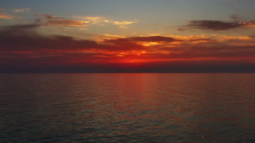 Aerial view of a vibrant sunset casting orange and red light over the calm waters of the Adriatic Sea, Montenegro.