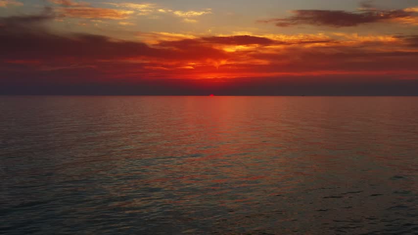 Aerial view of vibrant sunset over the calm sea with deep orange and red clouds reflecting on the water surface in Montenegro.