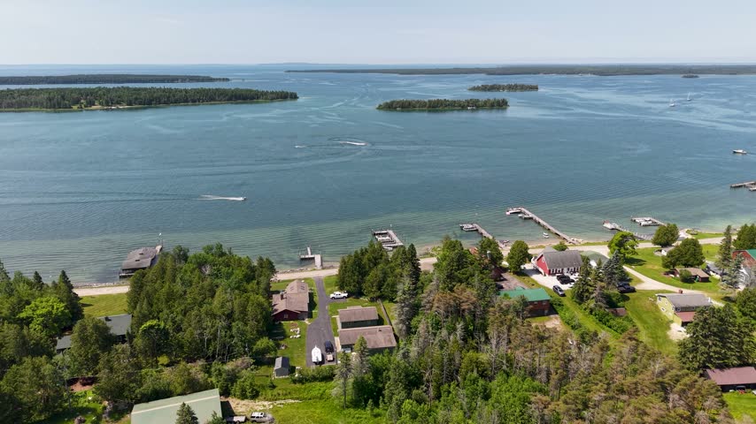 Aerial view of motorboats leaving white wakes between Lake Huron islands above waterfront homes and docks in Hessel Michigan.