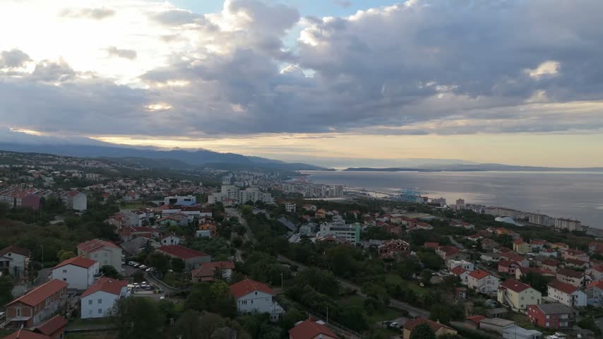 Aerial view of the coastal city of Rijeka with residential buildings, lush greenery, and the Adriatic Sea under a cloudy sky in Rijeka, Primorje-Gorski Kotar, Croatia.