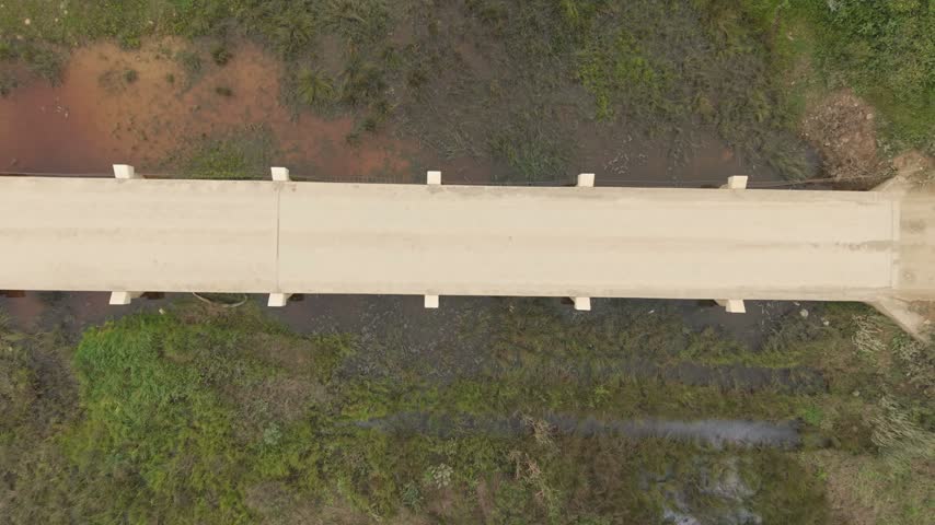 Aerial view of a cyclist riding across a concrete bridge over a stream surrounded by lush green wetlands in Greyton, Western Cape, South Africa.