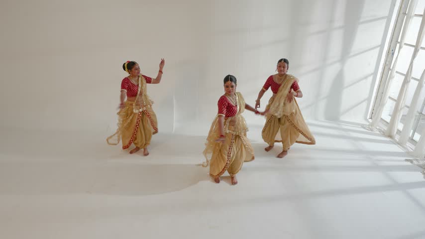 Three Indian women performing a traditional dance in a bright, spacious room