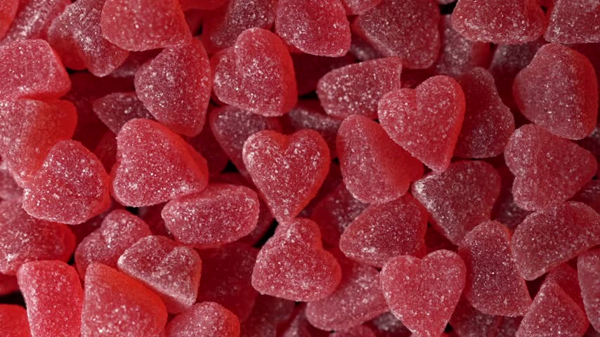 Macro close up of many red heart shaped jelly gummy candies covered in sugar grains stacked together in texture background for romantic themes and holiday celebrations like Valentines Day party events